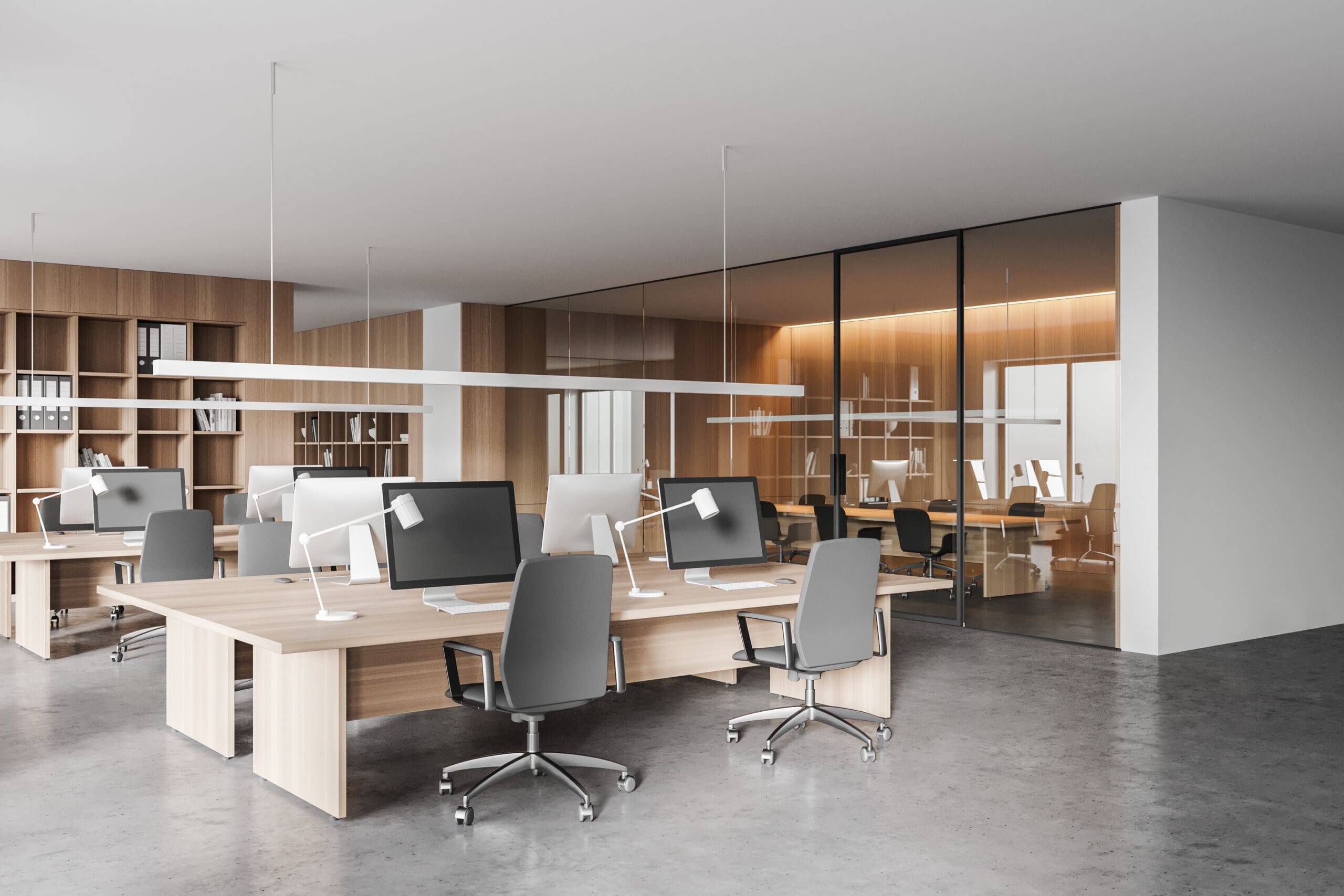 Modern office space with wooden desks arranged in rows, crafted through expert carpentry, each equipped with computers and ergonomic chairs. The room features large glass partitions, minimalistic design, and ample natural lighting.
