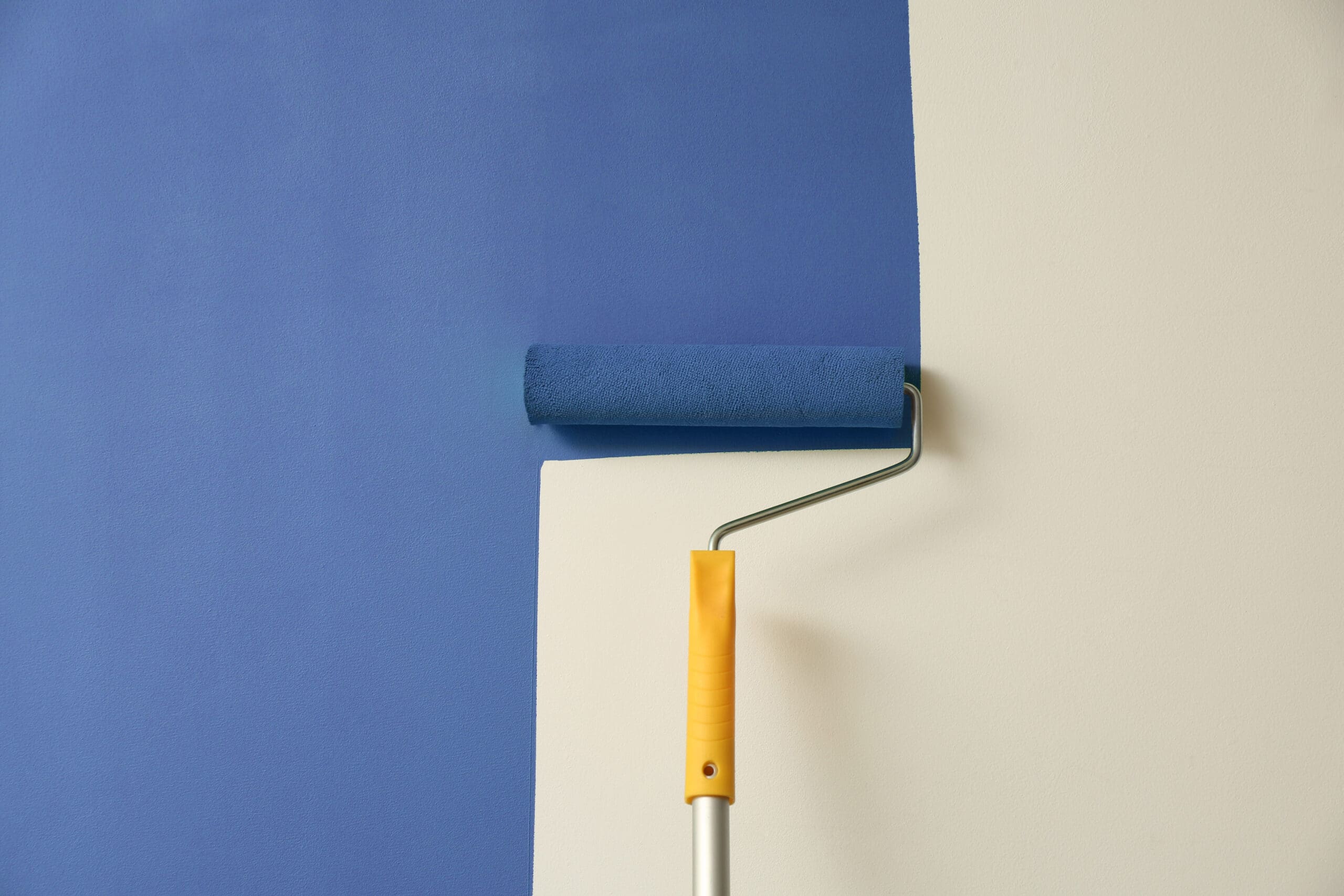 A paint roller with a yellow handle expertly applies a coat of blue paint, crafting a precise dividing line on the wall. Ideal for any dry lining contractor, this tool ensures seamless transitions and flawless finishes between colors.